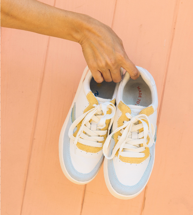 person holding colorful sneakers against orange wall